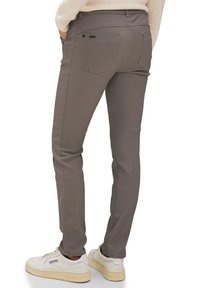 Grijze stretchbroeken met een slank ontwerp, voorzien van achterzakken en contrasterende stiksels, gecombineerd met witte sneakers.