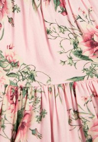 Tissu rose clair présentant un motif floral avec des roses et des feuilles. Le design inclut une texture froncée à l'ourlet avec des plis.