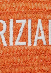 Material de paja trenzada naranja con texto bordado en blanco. La textura muestra un tejido apretado y estampado con un acabado suave.