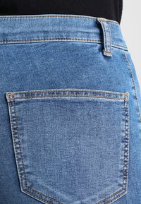 Jeans de mezclilla azul con un diseño de tiro medio, que cuentan con un bolsillo trasero con costura en contraste y una textura suave.