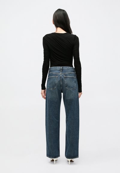 Μαύρο τοπ με μακριά μανίκια συνδυασμένο με ψηλόμεσα, φαρδιά μπλε τζιν παντελόνια. Τα τζιν έχουν κλασική υφή denim και πίσω τσέπες.