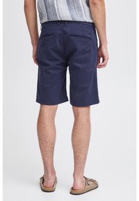 Shorts en coton bleu marine à coupe slim, dotés de deux poches arrière et d'une texture subtile. Portés avec des sandales décontractées et un haut à motifs.