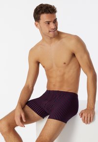 Boxer briefs da uomo a righe navy con linee rosse, caratterizzati da un design aderente e una cintura elastica, mostrati su un modello maschile seduto.