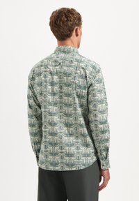 Groen gestippeld shirt met een geometrisch ontwerp, lange mouwen, een standaardkraag en een gebogen zoom. De stof heeft een gladde textuur.