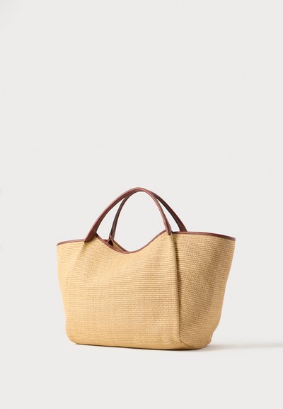 Τσάντα tote από πλεκτό ταμπά με καφέ δερμάτινες λαβές και διακοσμητικά, σε όρθια θέση σε λευκό φόντο.