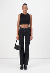 Black cropped tank top paired with high-waisted black jeans. Accessories include a small black handbag and ankle boots. Smooth texture.