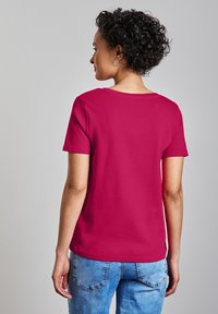 Fuchsiarosa t-shirt med kort ärm och rund halsringning, tillverkad av mjukt bomullstyg, i kombination med ljusblå denimjeans.