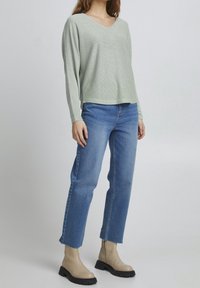 Hellgrüner strukturierter Strickpullover mit V-Ausschnitt, kombiniert mit blauen geraden Jeans und beigen Knöchelstiefeln mit dicken Sohlen.