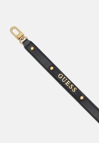 Lanière de porte-clés en cuir noir avec fermeture métallique dorée et clous dorés, avec le mot "GUESS" en lettres dorées.