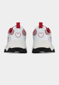 Λευκά και κόκκινα αθλητικά παπούτσια με μαύρες σόλες, διακοσμημένα με κόκκινα σχέδια καρδιάς στο πίσω μέρος και κόκκινες θηλιές πάνω από τις φτέρνες.