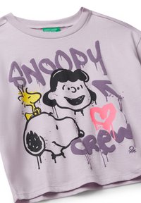 Světle fialové tričko s krátkým rukávem se černými a žlutými kreslenými motivy Snoopyho a Woodstoka, s růžovým textem ve stylu graffiti "SNOOPY CREW."
