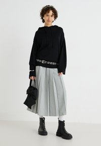 Sudadera negra de gran tamaño con cordón, combinada con una falda plisada de color gris claro y botas de tobillo negras con cremallera. Bolso negro con detalle de lazo.