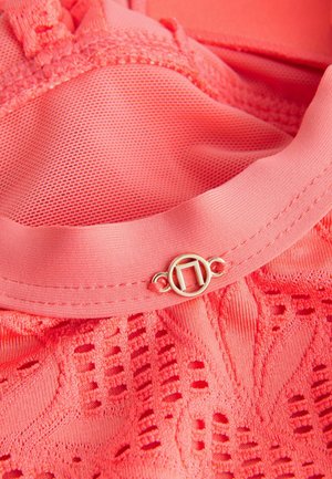 Koralfarvet stof med nettekstur og blonde detaljer. Har en clasp i guldfarve med et cirkulært design. Glat finish generelt.