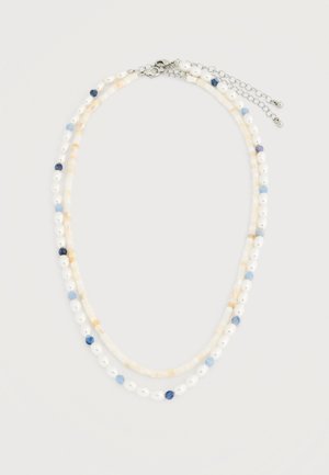 Collier à double rangée avec des perles blanches et beige clair, agrémenté de petites perles bleu clair et bleu foncé, fermé par un fermoir en argent et une chaîne réglable.