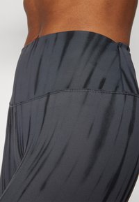 Leggings deportivos de cintura alta en gris oscuro, usados por una persona con costura lateral visible y textura de tela elástica suave.