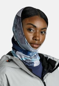 Gaiter de cuello Buff multicolor con un estampado abstracto de montañas, hecho de un tejido elástico. Lleva puesto debajo de una chaqueta gris con cremallera.