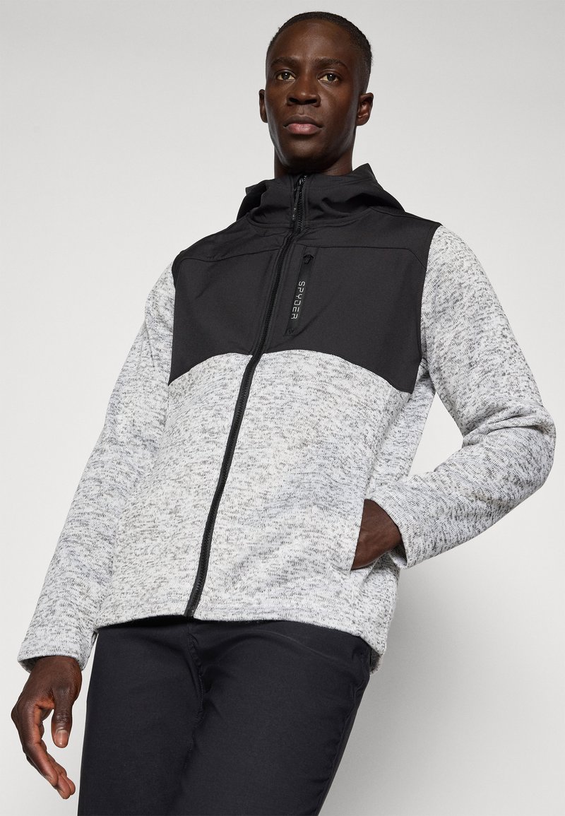 Veste zippée pour homme avec un panneau supérieur noir et une section inférieure gris clair chiné, dotée d'une finition texturée et de poches latérales.