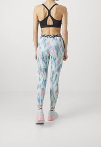 Reggiseno sportivo nero con schiena incrociata, abbinato a leggins blu pastello con motivi astratti in rosa e verde, e sneakers grigie.