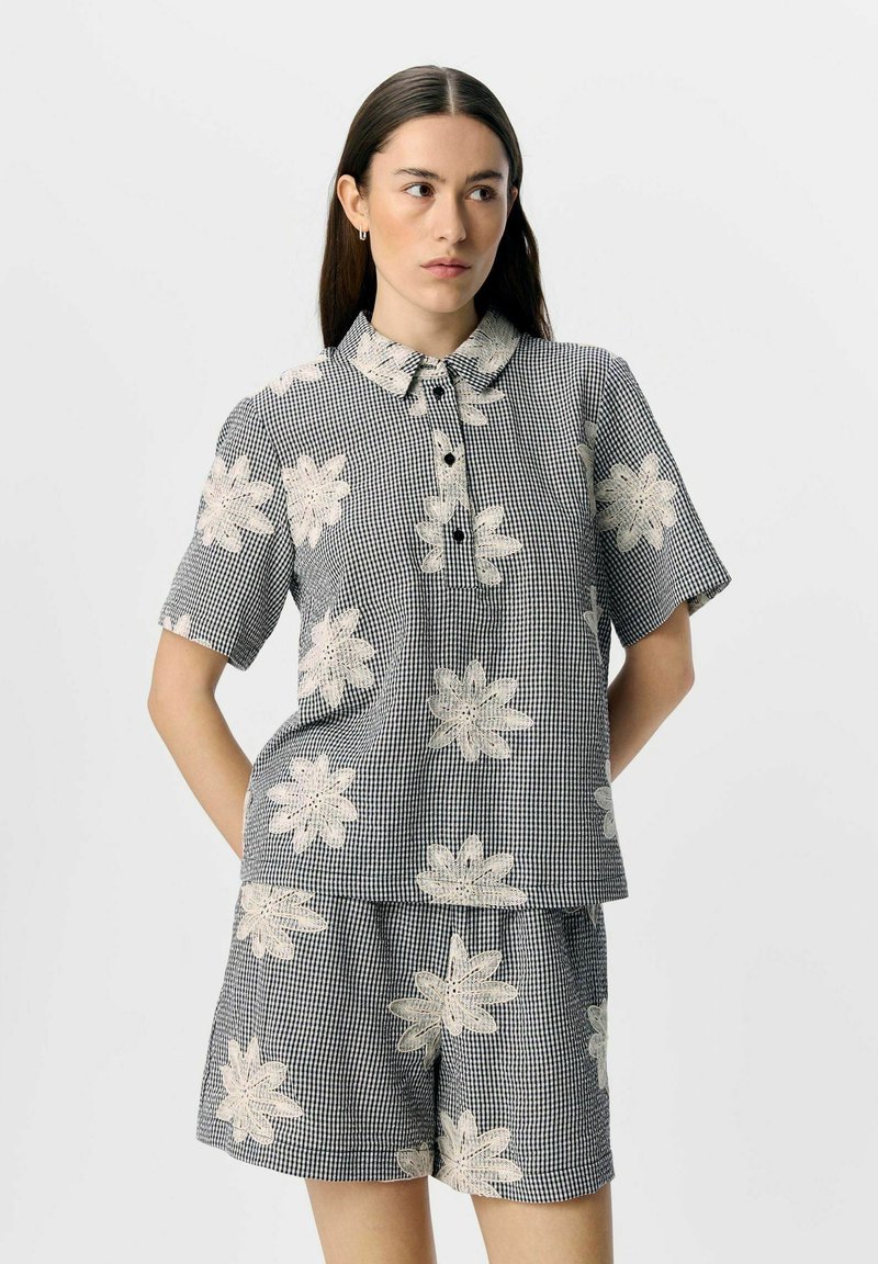 Chemise à manches courtes à carreaux noir et blanc avec broderie florale, dotée d'un col et d'une patte de boutonnage, associée à un short assorti.