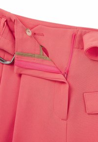 Růžové kalhoty na míru se zipovou kapsou a zapínáním na knoflík, s hladkou texturou a čistým prošíváním. Ozdobené kovovým kroužkem.