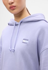 Világoslila kapucnis pulóver, a mellen "TOMMY JEANS" felirattal ellátott folttal, nyakkivágásnál húzózsinórokkal és puha tapintású anyaggal.