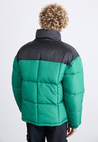 Chaqueta tipo puff con una sección superior negra y una sección inferior verde vibrante, con un diseño acolchado y un cuello alto.