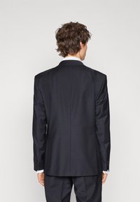 Dark navy suit jacket featuring notched lapels, single vent, and contrasting white shirt cuffs visible at the wrists. Smooth fabric texture.