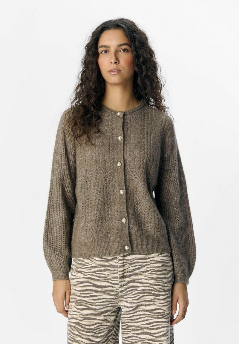 Brun stickad cardigan med rund hals, knappar framtill och strukturerade mönster. Långa ärmar gjorda av mjukt garn, tillsammans med randiga byxor.