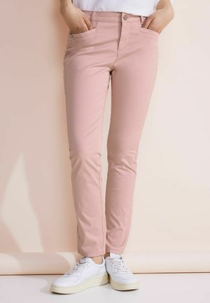 Jasnoróżowe skinny pants wykonane z gładkiego materiału, z przednimi kieszeniami i zapięciem na guzik, w połączeniu z białymi trampkami.