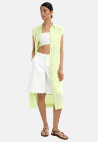 Jasnozielona, przezroczysta koszula zapinana na guziki, nałożona na białą crop top i białe szorty. Szorty mają długość do kolan i klasyczny krój. Brązowe klapki.