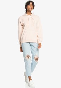 Light pink hooded sweatshirt with "ROXY" printed in a slightly raised texture, paired with distressed light blue jeans and white sneakers.