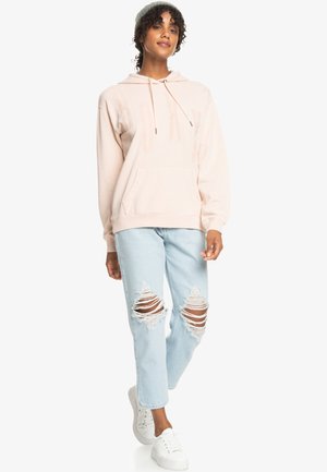 Light pink hooded sweatshirt with "ROXY" printed in a slightly raised texture, paired with distressed light blue jeans and white sneakers.