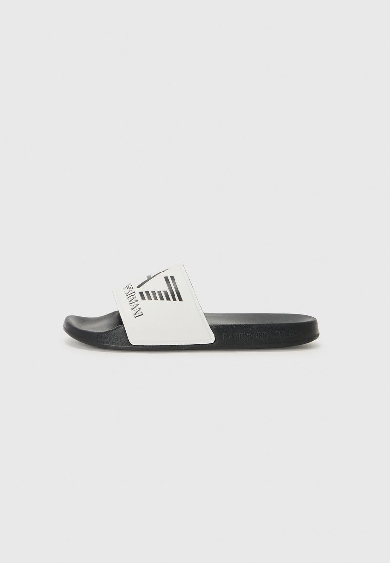 Svart glidesandal med hvit overdel som har logo og stripete design. Flat såle og glatt tekstur for avslappet bruk.