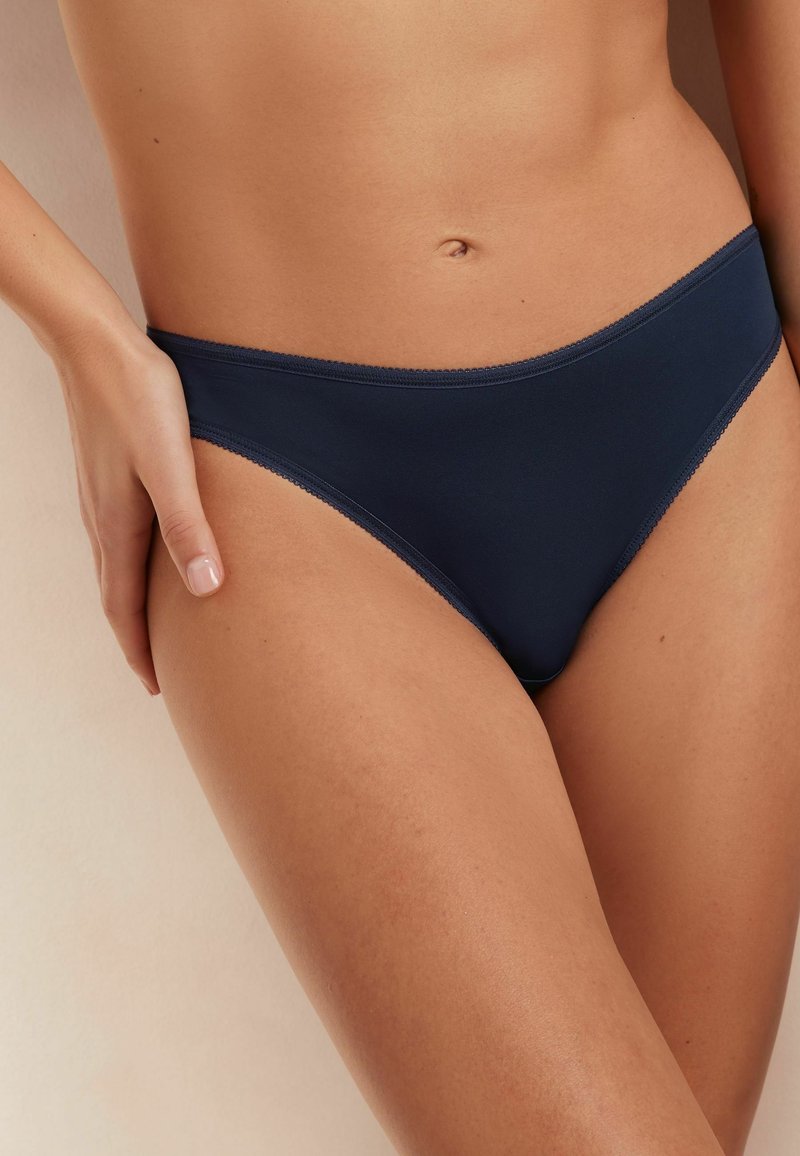 Marineblauwe bikini slips van een gladde, rekbare stof met fijne kantafwerking langs de randen. Ontworpen voor een minimale dekking.