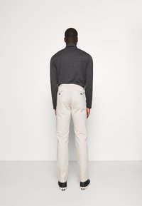 Herenoutfit bestaande uit een donkergrijs langemouwen shirt en beige broek, met een gladde textuur en minimale details. Achteraanzicht gepresenteerd.
