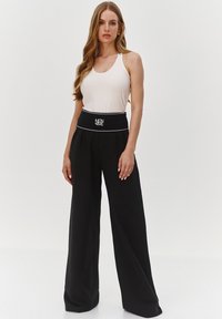 Czarne spodnie w szerokim kroju z wysokim stanem, z białym logo i lamówką. W komplecie z dopasowanym, jasnobeżowym topem bez rękawów. Gładka faktura materiału.