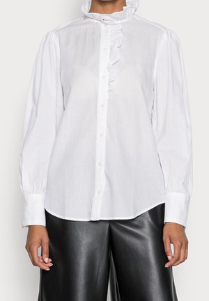 Biała bluzka z długim rękawem z falbankowatym, wysokim kołnierzem i zapięciem z przodu, noszona z czarnymi skórzanymi spodniami o szerokich nogawkach.