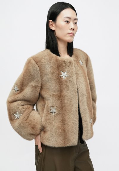 Kergepruun faux-fur jakk, millel on ümmargune kaelus. Varrukatel on tähtaplikatsioonid, mis on kaunistatud rhinestone'idega. Pehme tekstuur ja volüümikas sobivus.
