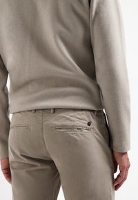 Grijze gebreide trui met een relaxte pasvorm, gecombineerd met lichtgrijze chino's met twee achterzakken en een klein logo-accent bij de taille.