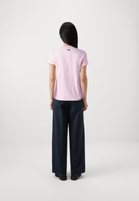 Camiseta de algodón de color rosa claro con mangas cortas y escote redondo. Presenta un pequeño logo negro en la parte posterior. Combinada con pantalones anchos de color azul marino.