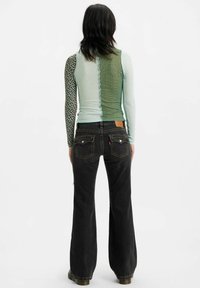 Top de manga larga con un diseño de patchwork: patrones en verde claro, verde oscuro y negro. Combinado con jeans oscuros de campana. Se muestra vista trasera.