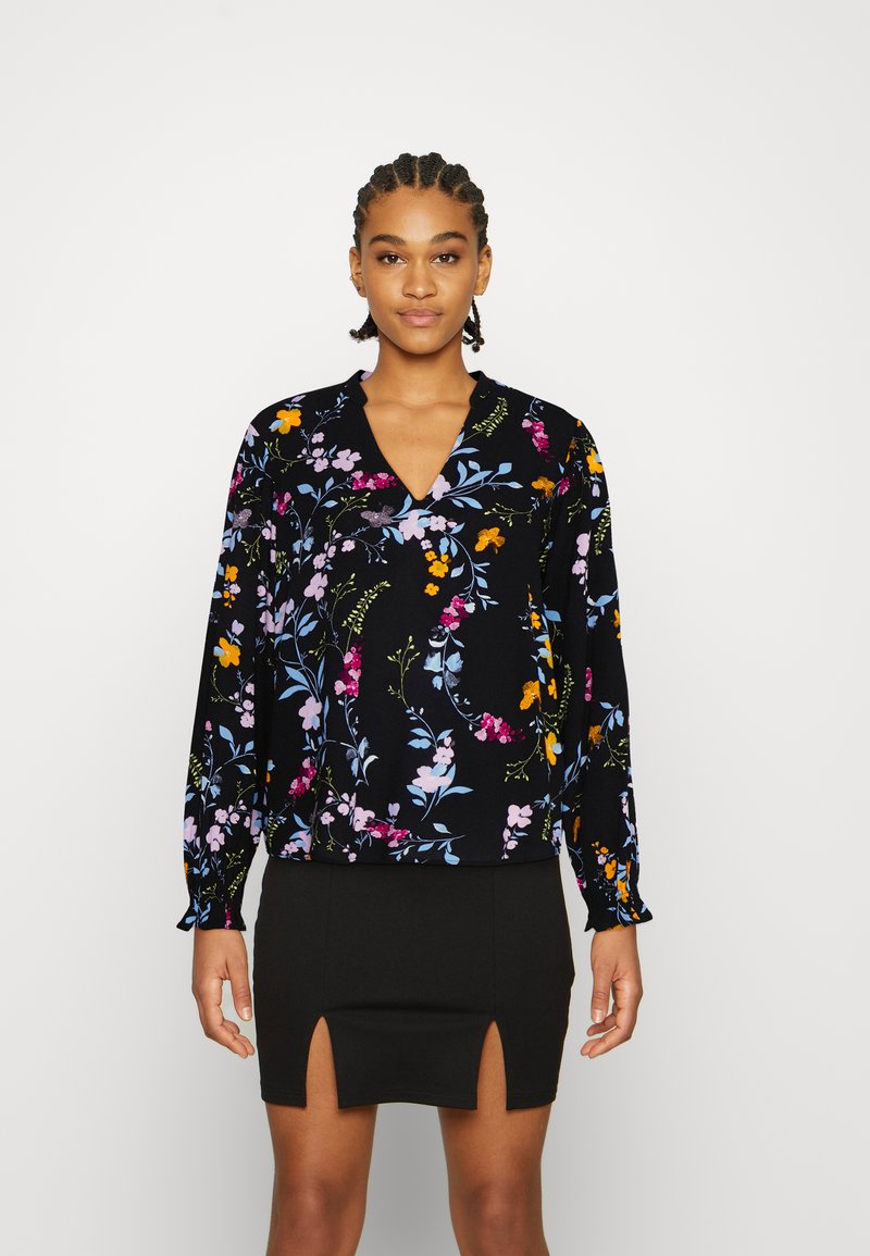 Blusa floral com fundo preto, apresentando mangas longas, decote em V e padrões florais coloridos em tons de rosa, amarelo e azul.