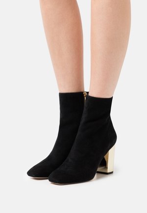 Stivaletti alla caviglia in suede nero con punta appuntita e tacco spesso, testurizzato, in oro metallico. Presentano una cerniera dorata sul retro.