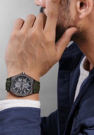 Uhr mit grünem Silikonarmband und silberfarbenem Metallgehäuse, ausgestattet mit einem detaillierten grauen Zifferblatt, das kontrastreiche schwarze und silberne Akzente aufweist.