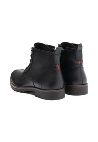 Botas de cuero negras hasta el tobillo con acabado texturizado, punta redonda, cierre de cordones en la parte frontal y tirador en la parte trasera. Presentan un acento rojo contrastante en el talón.