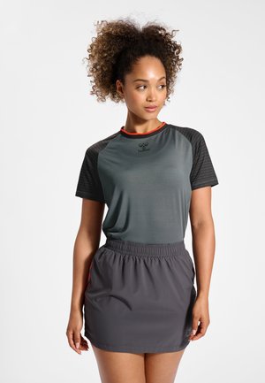 Leichtes graues Sporttop mit schwarzen gemusterten Ärmeln und roten Akzenten, kombiniert mit einem grauen Rock mit elastischem Bund.