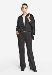 Pantaloni neri sartoriali con una vestibilità a gamba dritta, abbinati a una blusa nera e a un top di colore chiaro. Presentano una cintura con fibbia circolare.