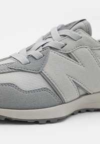 Zbliżenie na szare zamszowe i siateczkowe sneakersy z fakturowanymi sznurówkami i wypukłym logo z boku, umieszczone na białym tle.