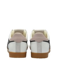 Zapatillas blancas y negras con acentos en gris y rosa, materiales de cuero y ante lisos, suelas de goma texturizada, cuellos acolchados.