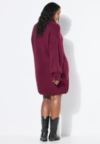 Burgunderfarbener, übergroßer Strickpullover mit puffigen Ärmeln, gerippten Bündchen und Saum. Kombiniert mit schwarzen Cowboystiefeln mit dekorativen Nähten.